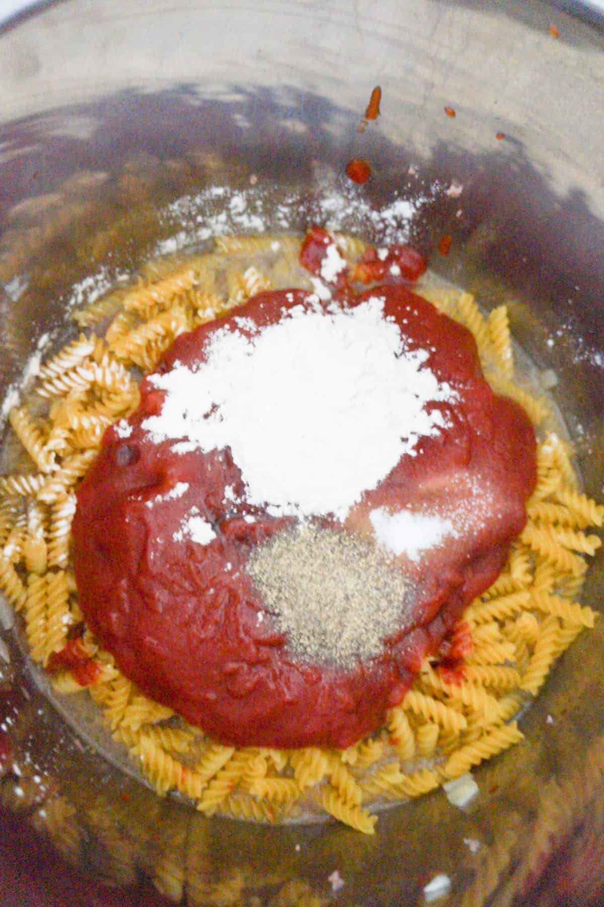 onion powder, pepper and ketchup on top of uncooked fusilli noodles in an Instant Pot