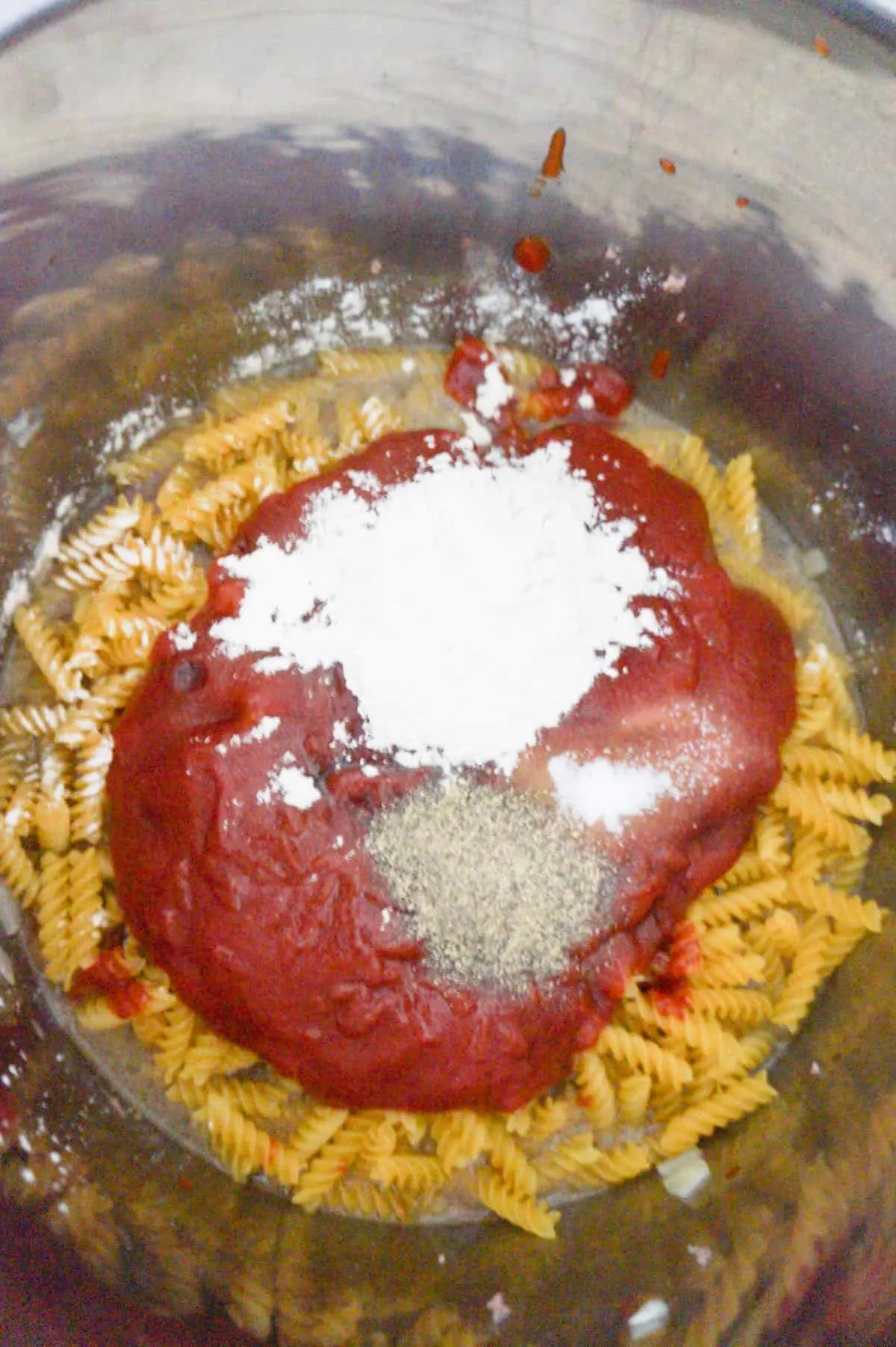 onion powder, pepper and ketchup on top of uncooked fusilli noodles in an Instant Pot