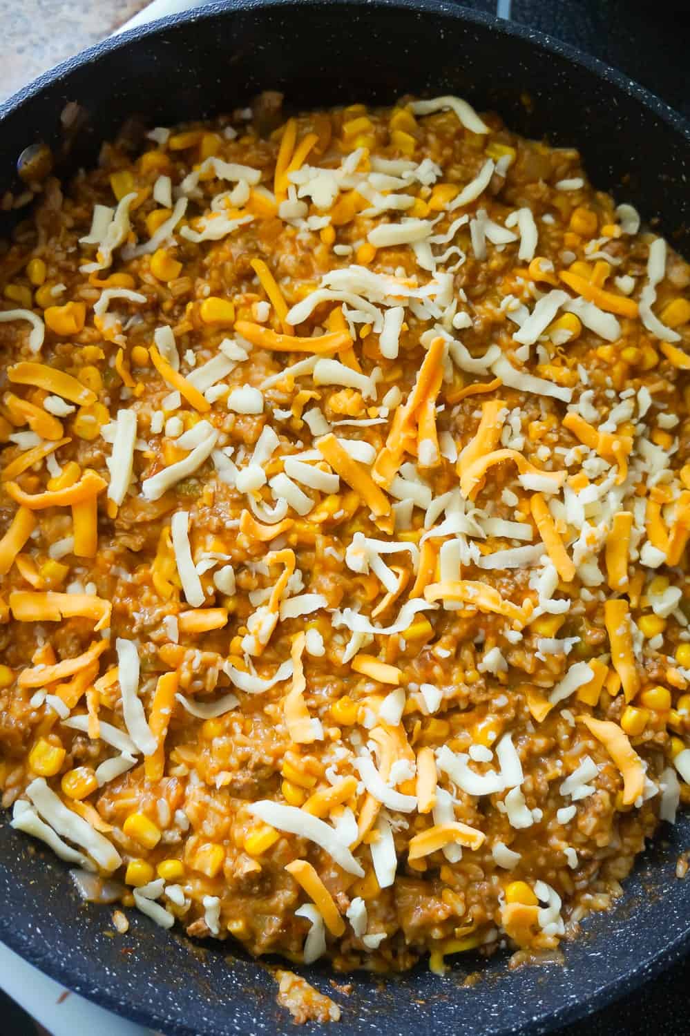 shredded mozzarella and cheddar on top of ground beef and rice in a skillet