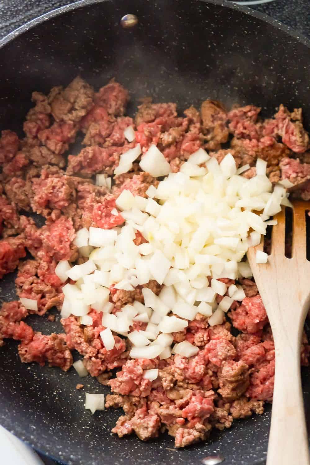 diced onions on top of raw ground beef in a frying pan