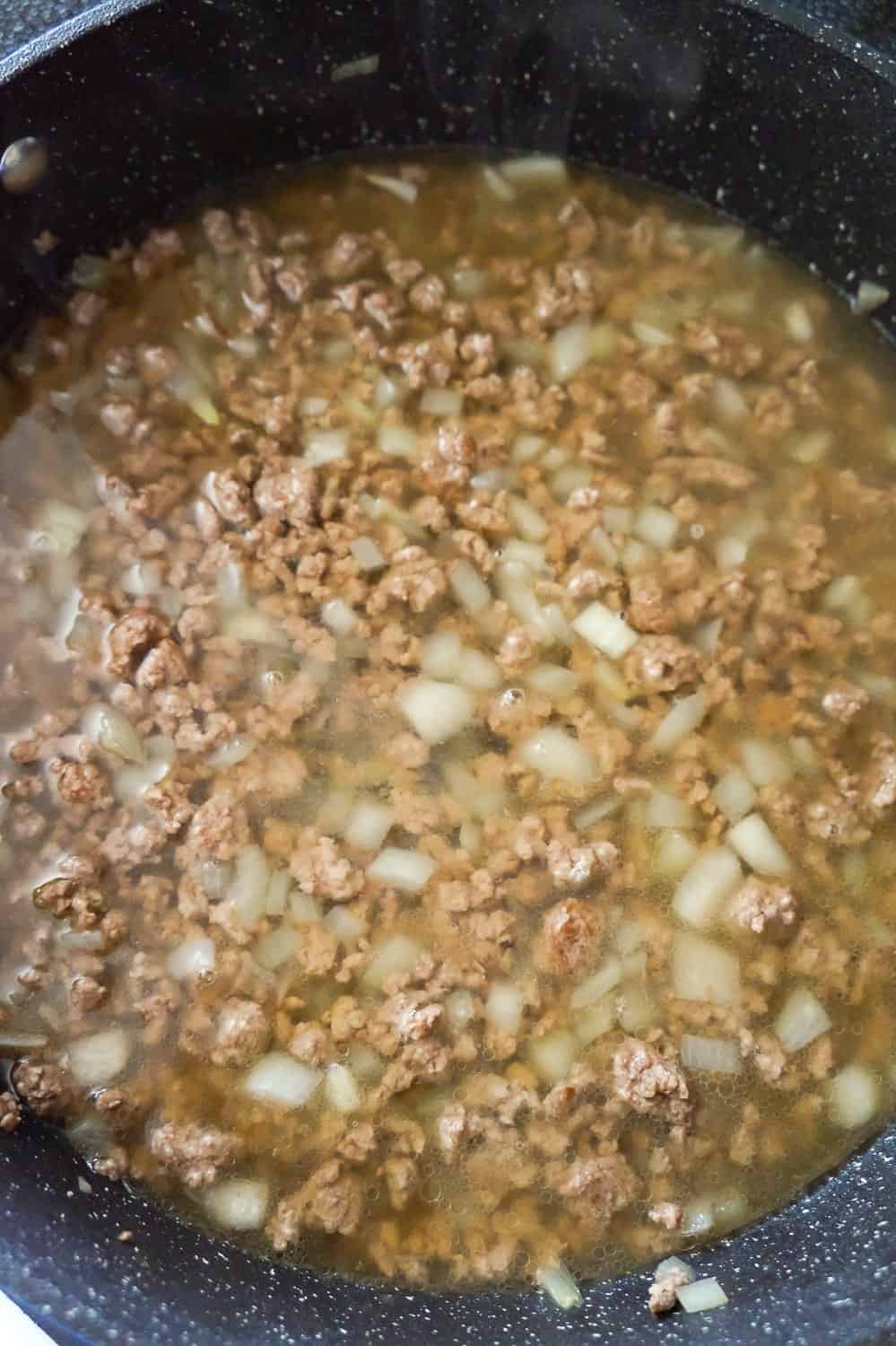 cooked ground beef and diced onions with chicken broth in a skillet